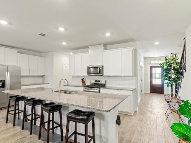 kitchen featuring white cabinets, a kitchen island with sink, sink, and appliances with stainless steel finishes