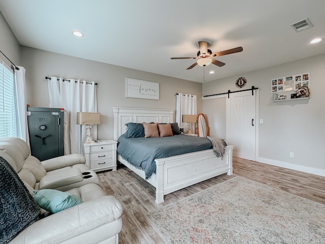 bedroom with a barn door, ceiling fan, and light wood-type flooring