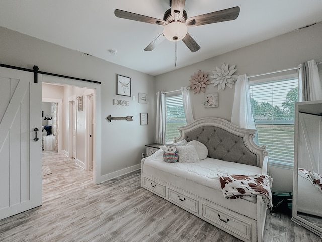 bedroom featuring a barn door, ceiling fan, and light wood-type flooring