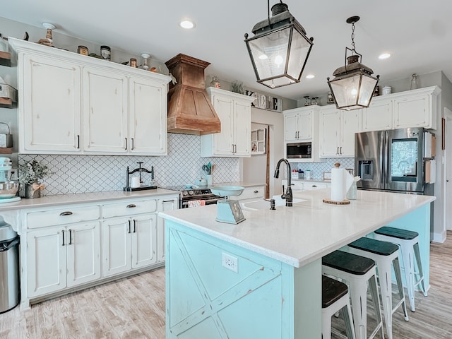 kitchen with premium range hood, sink, appliances with stainless steel finishes, a center island with sink, and white cabinets