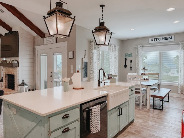 kitchen with a fireplace, a center island with sink, light hardwood / wood-style floors, stainless steel dishwasher, and vaulted ceiling with beams