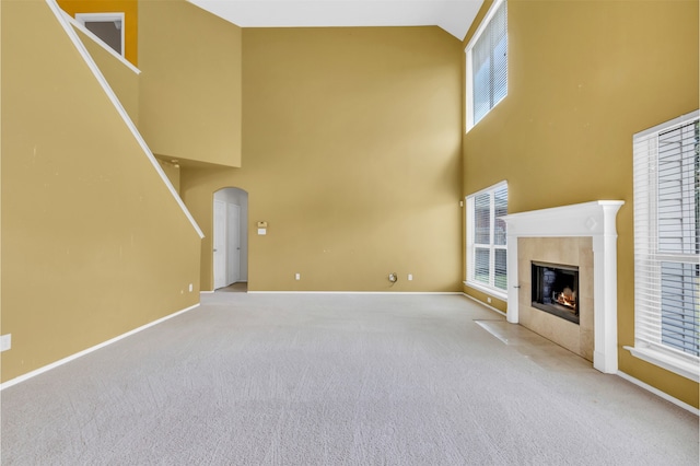 unfurnished living room with a towering ceiling, carpet floors, and a tile fireplace