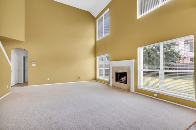 unfurnished living room with a tiled fireplace, light carpet, and high vaulted ceiling