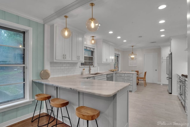 kitchen featuring sink, a kitchen breakfast bar, kitchen peninsula, decorative light fixtures, and white cabinets