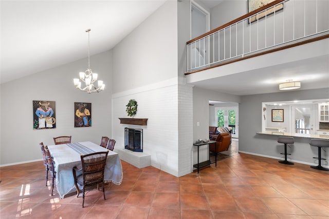 dining area with tile patterned flooring, high vaulted ceiling, a chandelier, and a brick fireplace