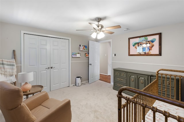 bedroom featuring light colored carpet, ceiling fan, a closet, and a crib