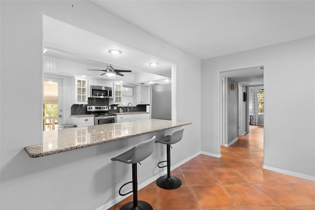 kitchen with stainless steel appliances, sink, ceiling fan, decorative backsplash, and white cabinets