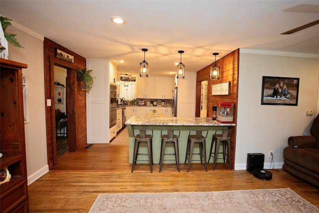 kitchen featuring white cabinetry, kitchen peninsula, light wood-type flooring, hanging light fixtures, and a breakfast bar area