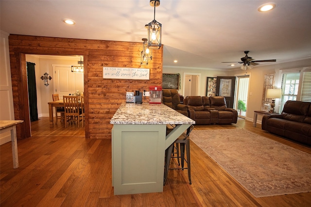 kitchen featuring pendant lighting, light stone counters, hardwood / wood-style flooring, a kitchen breakfast bar, and ceiling fan