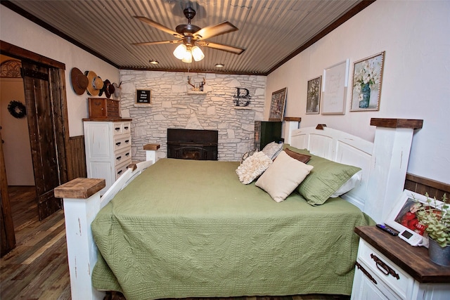 bedroom featuring wooden walls, a stone fireplace, wooden ceiling, dark hardwood / wood-style flooring, and ornamental molding