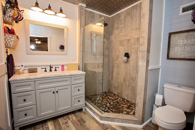 bathroom featuring toilet, a tile shower, wood-type flooring, vanity, and wooden walls