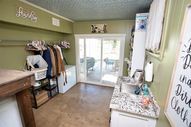 clothes washing area featuring ornamental molding, sink, a textured ceiling, and wooden walls