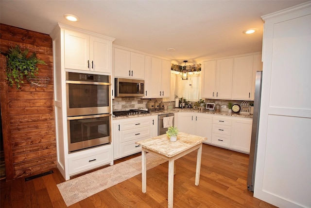 kitchen featuring white cabinets, stainless steel appliances, light stone counters, and hardwood / wood-style floors