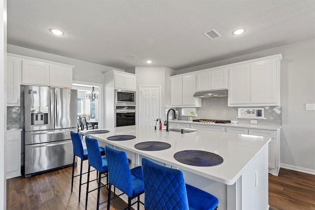 kitchen with dark wood-type flooring, appliances with stainless steel finishes, a kitchen breakfast bar, and a center island with sink