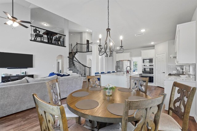 dining area with ceiling fan with notable chandelier, a high ceiling, and dark hardwood / wood-style floors