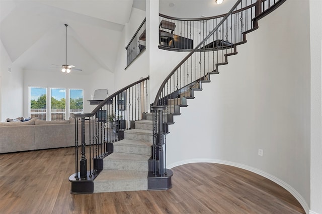 stairs featuring hardwood / wood-style floors, high vaulted ceiling, and ceiling fan