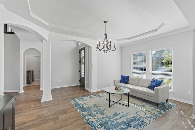 living room with ornamental molding, a tray ceiling, a notable chandelier, and hardwood / wood-style flooring