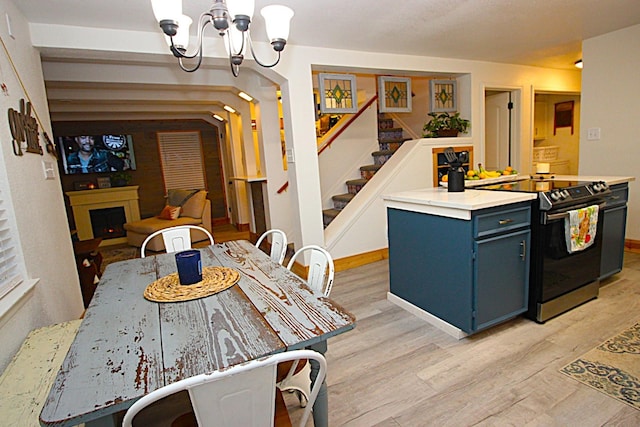 kitchen featuring a chandelier, light wood-style flooring, blue cabinets, a lit fireplace, and electric range oven