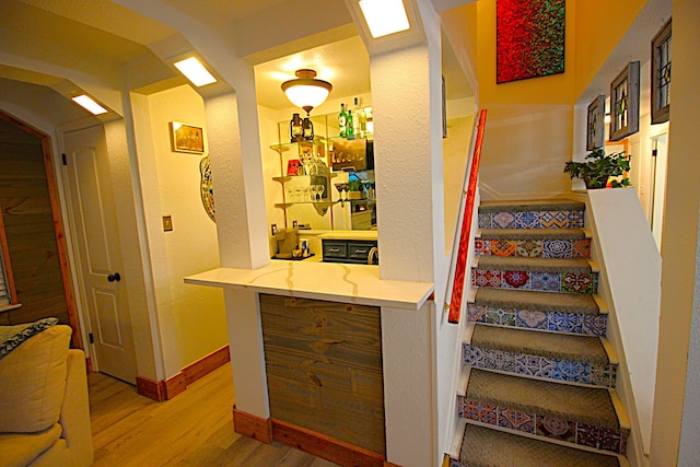 staircase with arched walkways, indoor wet bar, wood finished floors, and baseboards