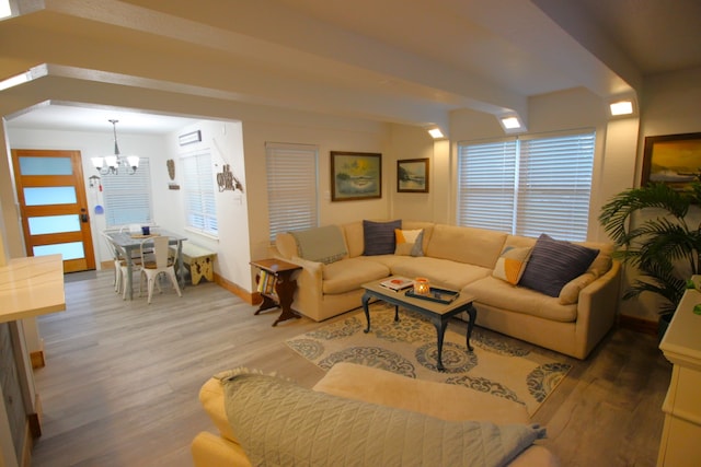 living room featuring a wealth of natural light, baseboards, wood finished floors, an inviting chandelier, and beam ceiling