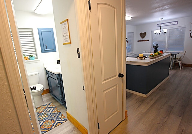 hall featuring an inviting chandelier, light wood-style flooring, and baseboards