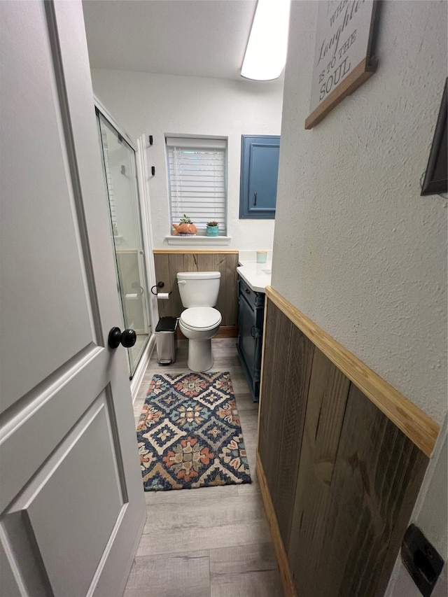 bathroom with vanity, wainscoting, wood finished floors, toilet, and a stall shower