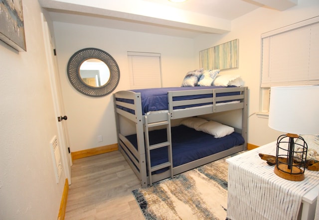 bedroom with beam ceiling, baseboards, and wood finished floors