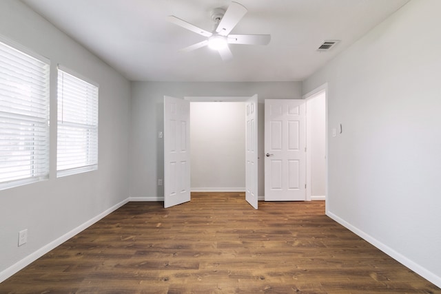 unfurnished bedroom with ceiling fan, multiple windows, and dark wood-type flooring