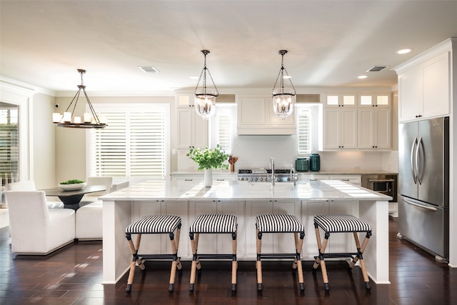 kitchen featuring appliances with stainless steel finishes, decorative light fixtures, white cabinetry, and an island with sink