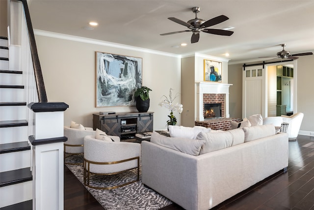 living room featuring a brick fireplace, ceiling fan, crown molding, dark wood-type flooring, and a barn door