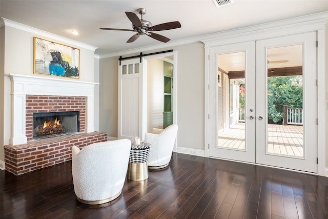 sitting room featuring crown molding, a brick fireplace, dark hardwood / wood-style floors, a barn door, and ceiling fan