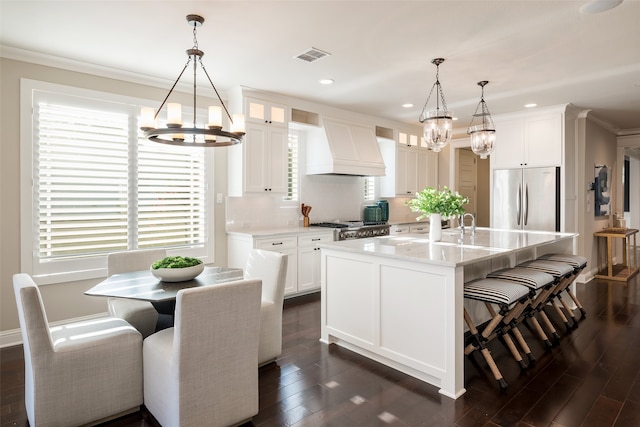 kitchen with appliances with stainless steel finishes, a center island with sink, dark hardwood / wood-style floors, white cabinetry, and hanging light fixtures