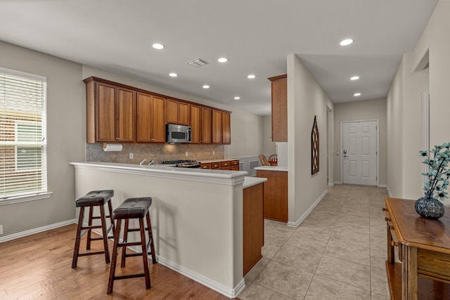 kitchen with backsplash, kitchen peninsula, a breakfast bar, and light tile patterned floors