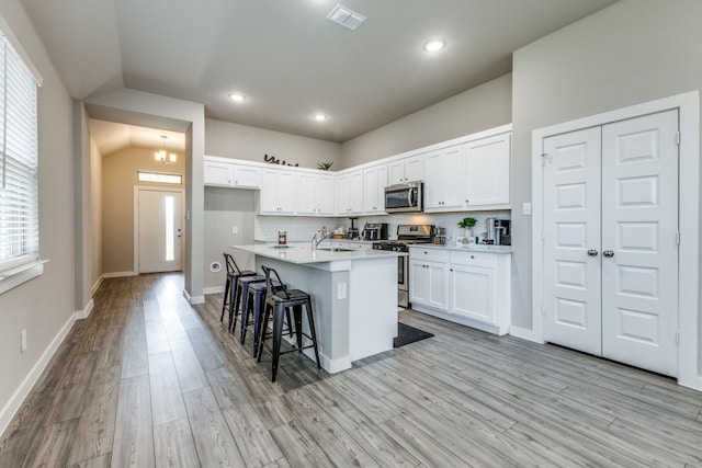 kitchen with white cabinetry, stainless steel appliances, a kitchen breakfast bar, and light hardwood / wood-style floors