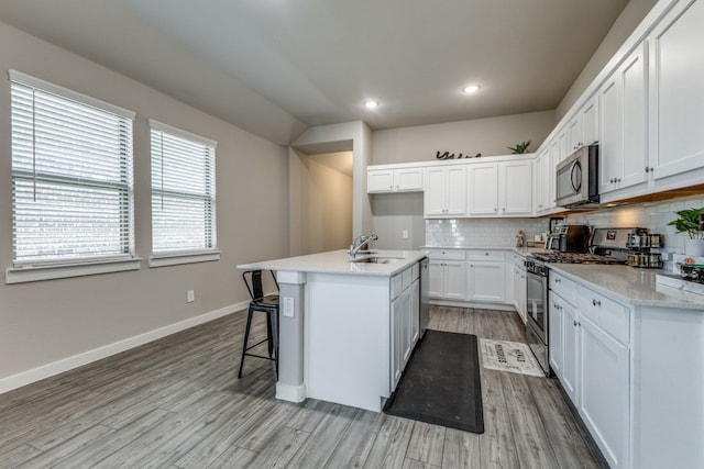 kitchen with appliances with stainless steel finishes, light hardwood / wood-style floors, white cabinetry, sink, and a kitchen island with sink