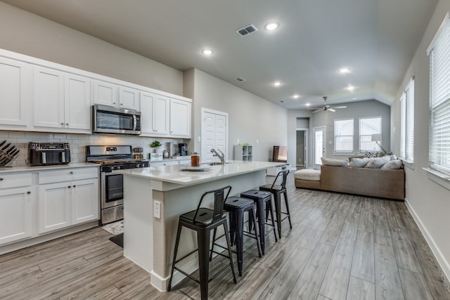 kitchen with stainless steel appliances, light hardwood / wood-style floors, an island with sink, ceiling fan, and a kitchen bar