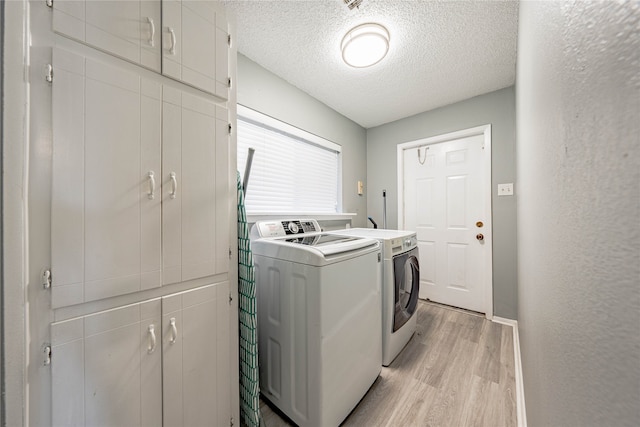 laundry room with cabinets, light wood-type flooring, a textured ceiling, and independent washer and dryer