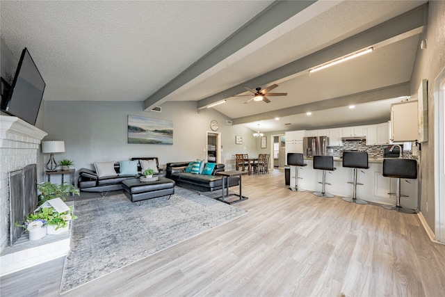 living room with a brick fireplace, light wood-type flooring, ceiling fan, vaulted ceiling with beams, and sink