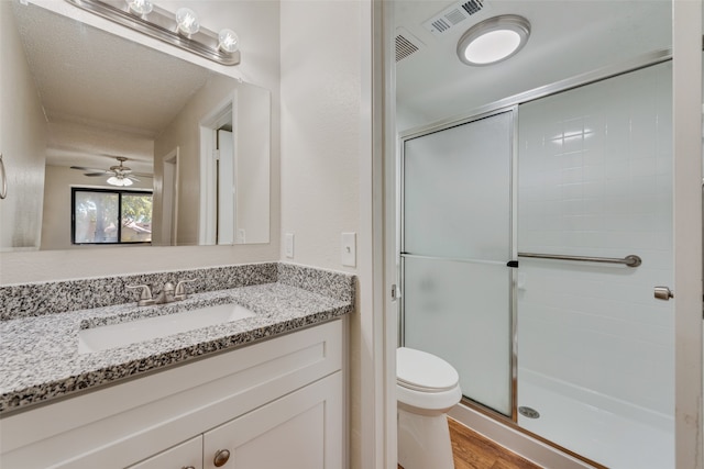 bathroom featuring a shower with door, hardwood / wood-style floors, toilet, ceiling fan, and vanity