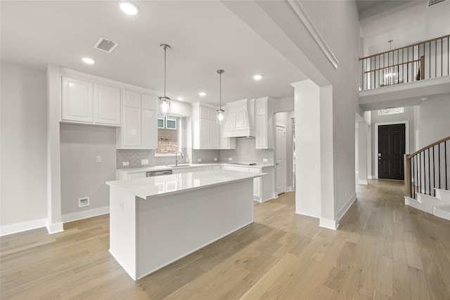 kitchen with hanging light fixtures, sink, a kitchen island, white cabinetry, and light hardwood / wood-style flooring