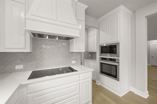 kitchen with stainless steel appliances, white cabinetry, light hardwood / wood-style flooring, premium range hood, and decorative backsplash