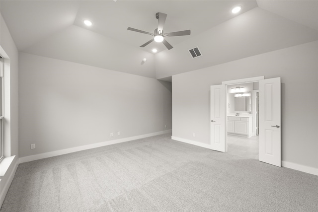 unfurnished bedroom featuring ceiling fan, ensuite bath, lofted ceiling, and light colored carpet