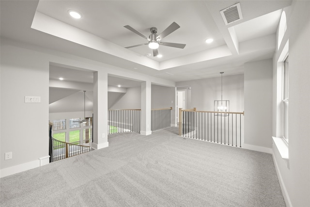 carpeted spare room featuring ceiling fan with notable chandelier and a raised ceiling