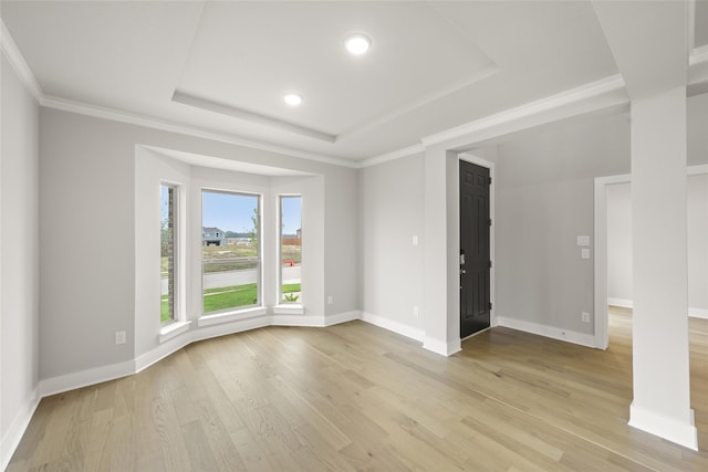 empty room featuring a raised ceiling, ornamental molding, and light hardwood / wood-style flooring