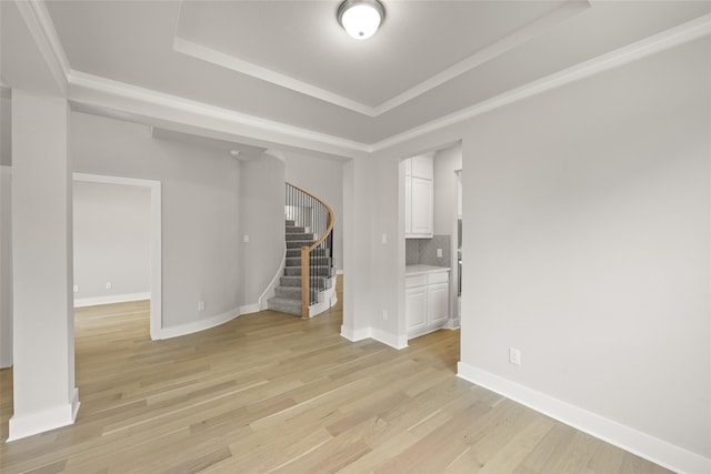 spare room featuring a raised ceiling, light wood-type flooring, and crown molding