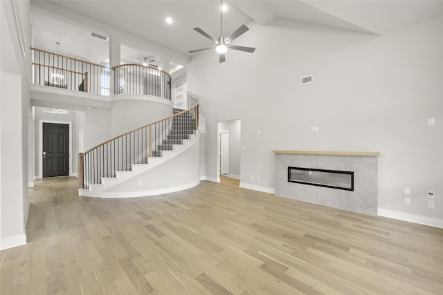 unfurnished living room featuring a high ceiling, a tile fireplace, ceiling fan, and light wood-type flooring