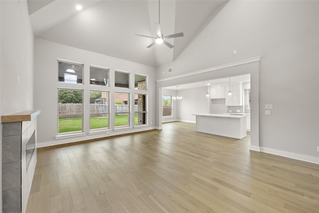 unfurnished living room with a fireplace, ceiling fan with notable chandelier, light wood-type flooring, and high vaulted ceiling