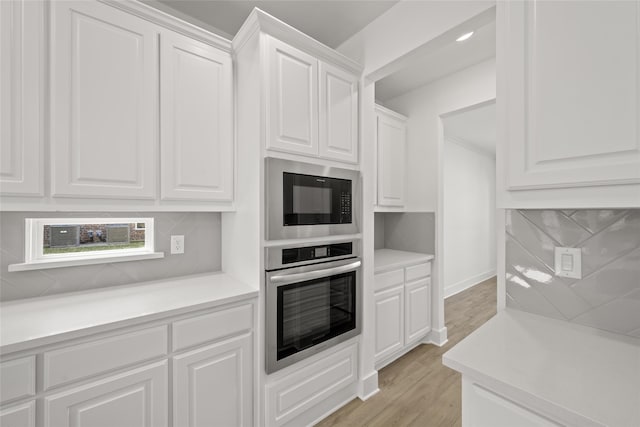 kitchen featuring decorative backsplash, light hardwood / wood-style floors, white cabinets, black microwave, and oven