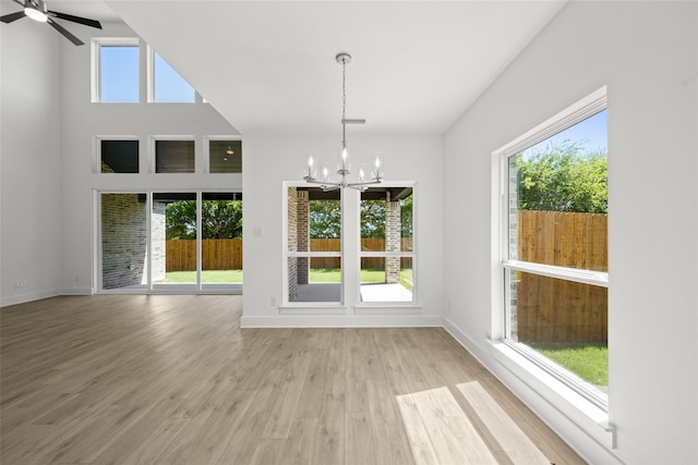 interior space featuring ceiling fan with notable chandelier, a towering ceiling, and light hardwood / wood-style flooring