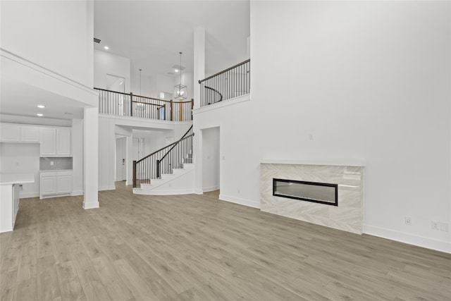 unfurnished living room with a fireplace, light wood-type flooring, and a high ceiling